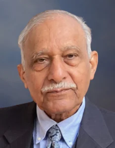 A distinguished elderly Pakistani man in a a suit and tie looks directly at the viewer.